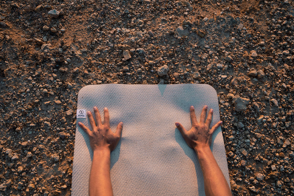 Gestreckte Hände auf Yogamatte auf steinigem Untergrund